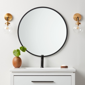 Black rubber framed round mirror hanging on bathroom wall above white vanity