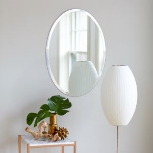 Frameless beveled oval copper-free mirror hanging on wall near lamp