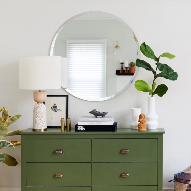 Frameless beveled edge round mirror mounted on the wall above a green credenza in a living room