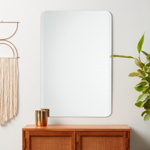 Frameless beveled rounded rectangle mirror hanging on wall above credenza