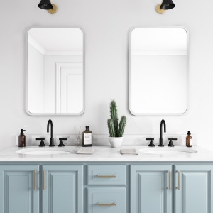 Two grey rubber framed rectangle mirrors hanging on bathroom wall above light blue double sink vanity