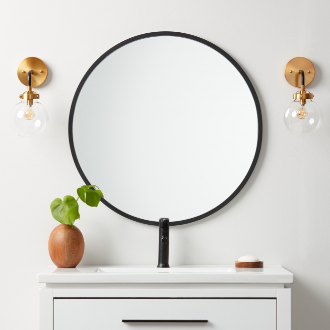 Black rubber framed round mirror hanging on bathroom wall above vanity