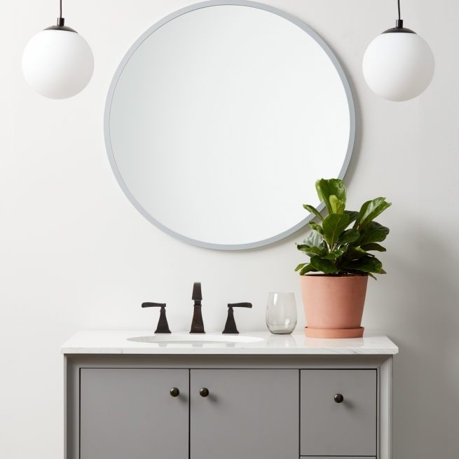 Grey rubber framed round mirror hanging on bathroom wall above vanity