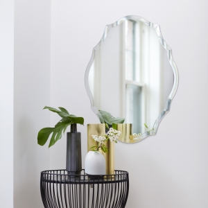 Frameless scalloped oval mirror hanging on wall near side table
