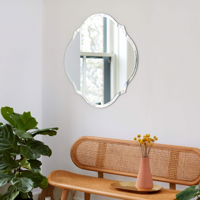Frameless scalloped round mirror hanging on wall above bench and plant